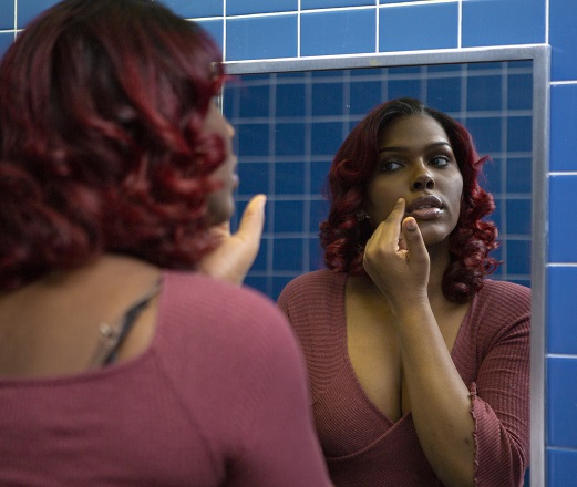 A young transgender woman looking at her face in the bathroom mirror