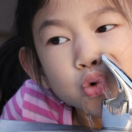 young girl drinking water from water fountain