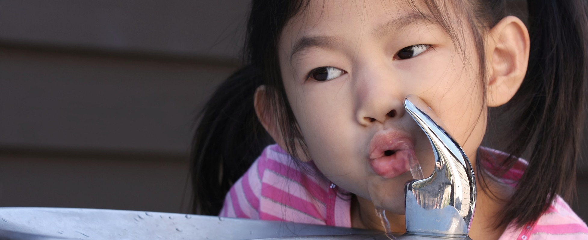 young girl drinking water from water fountain