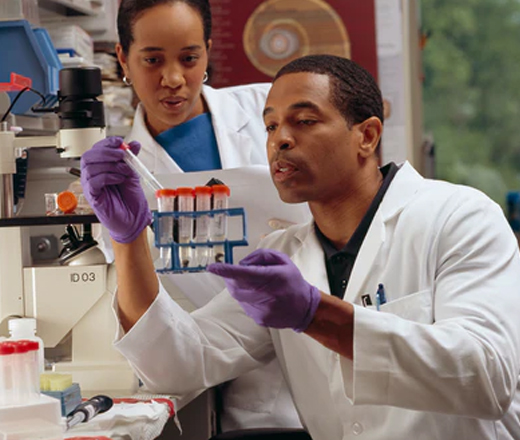 A male researcher checks test tubes as a female cancer researcher looks