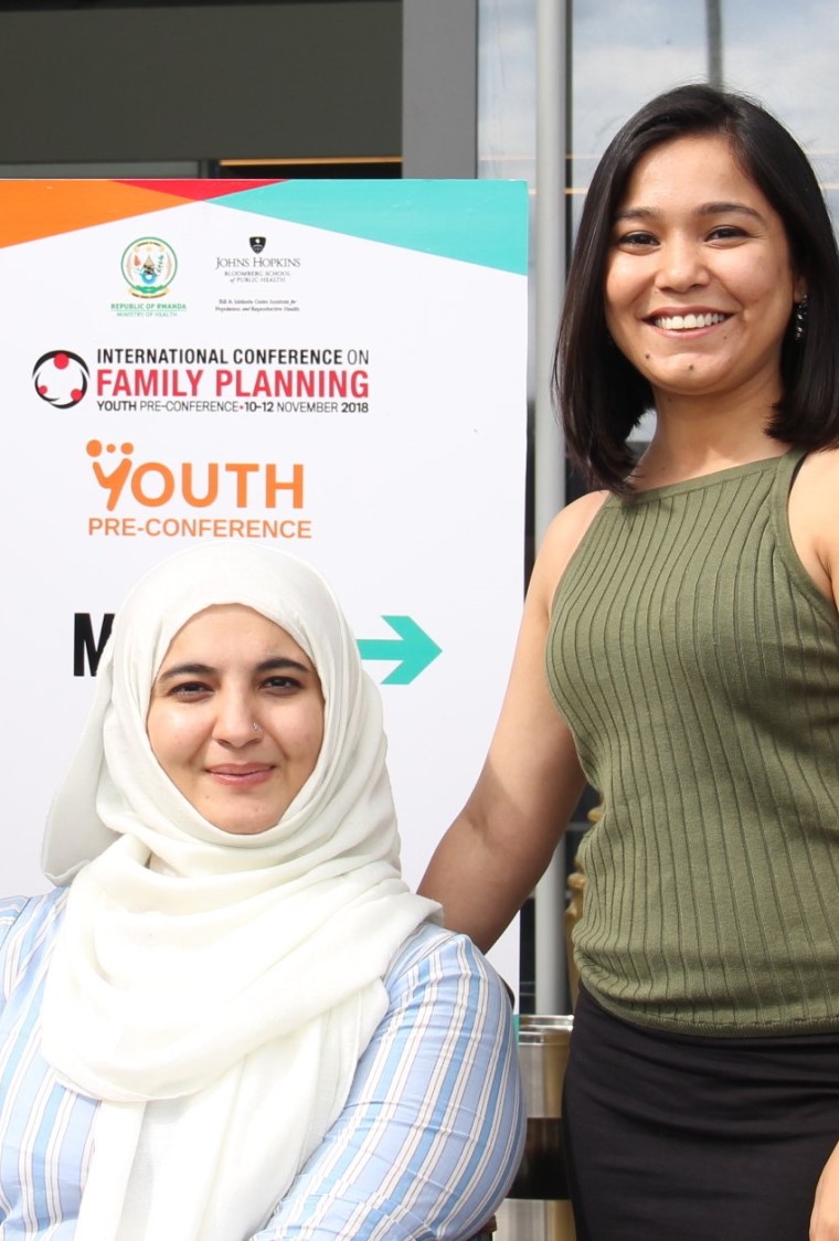 two women smiling in front of a family planning poster
