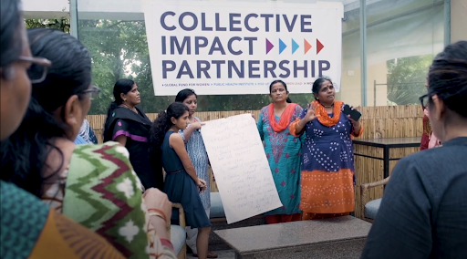 Women speaking to a crowd, standing in front of a sign that reads "Collective Impact Partners"