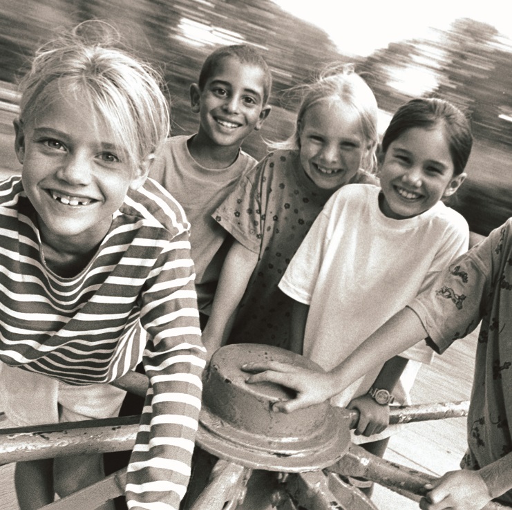 Black and white image of kids on a merry go round, smiling at camera