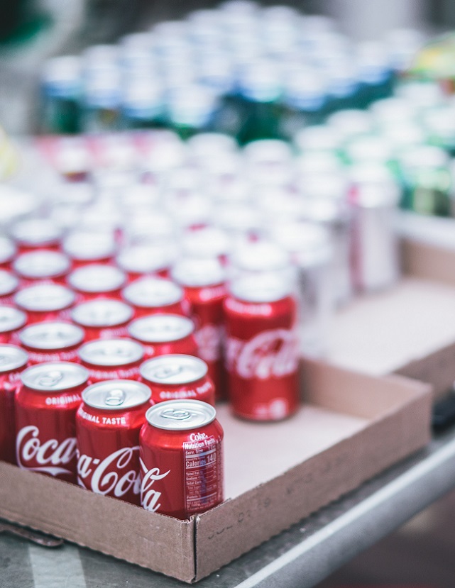 Selective focus shot of red Coca-Cola can lot in boxes, with other soda cans in the background