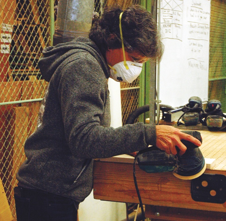 Man in woodshop, cutting wood while wearing safety equipement