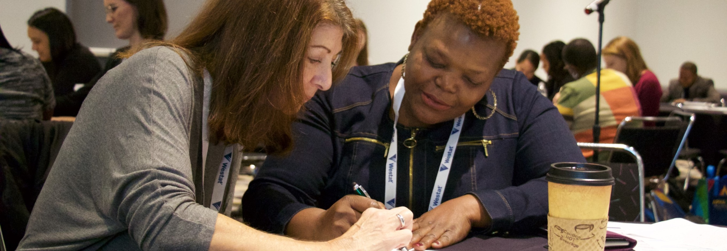 two women seated at a table, working on an application together.