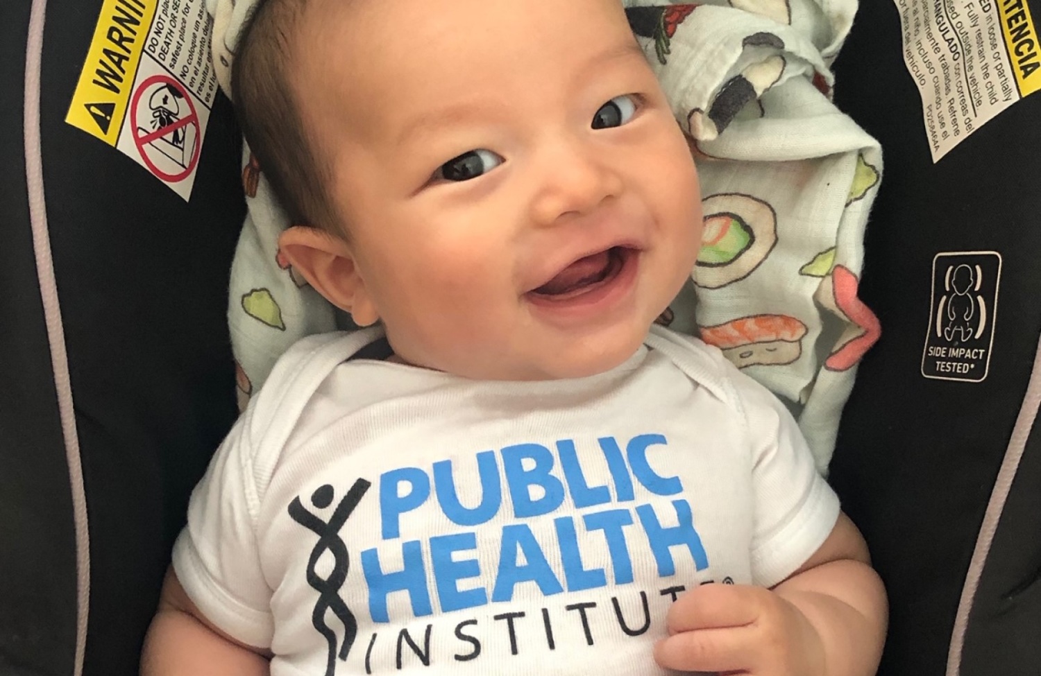 infant wearing a phi onesie, smiling at camera
