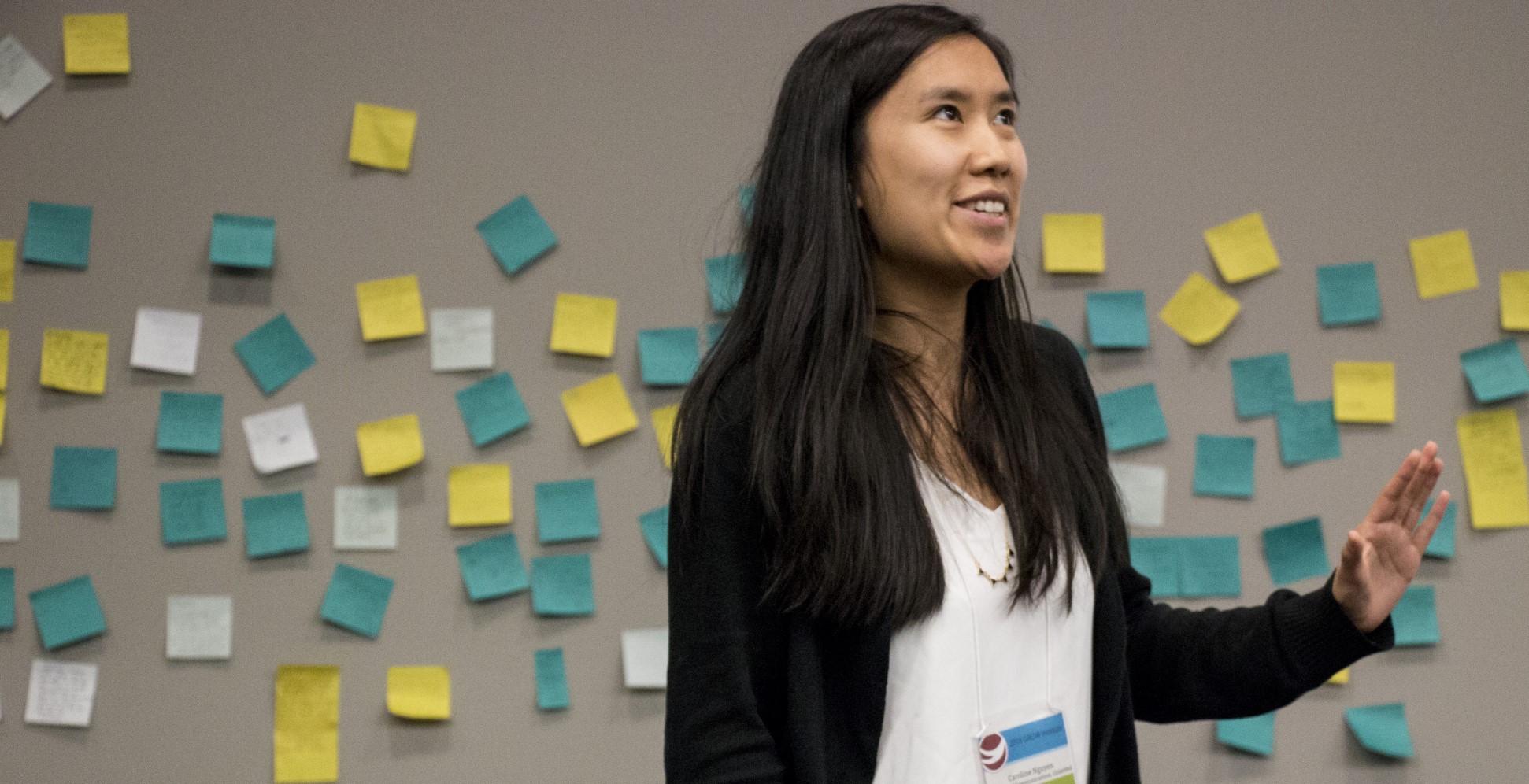 Woman from the waist up, looking off camera. A wall covered with post-its behind her.