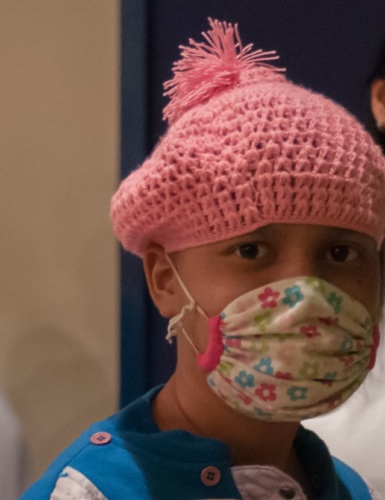 young person with knit cap covering hair loss from chemo, from the shoulders up, wearing mask