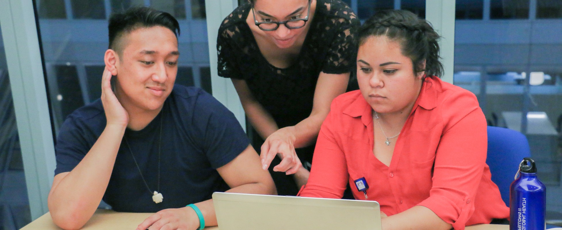 Three people, looking at a compter screen together, two sitting and one standing