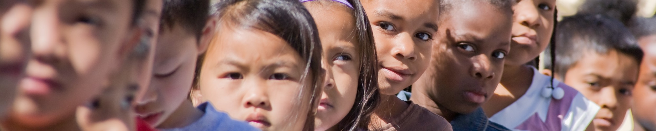 young children standing in a line, one girl peeping out