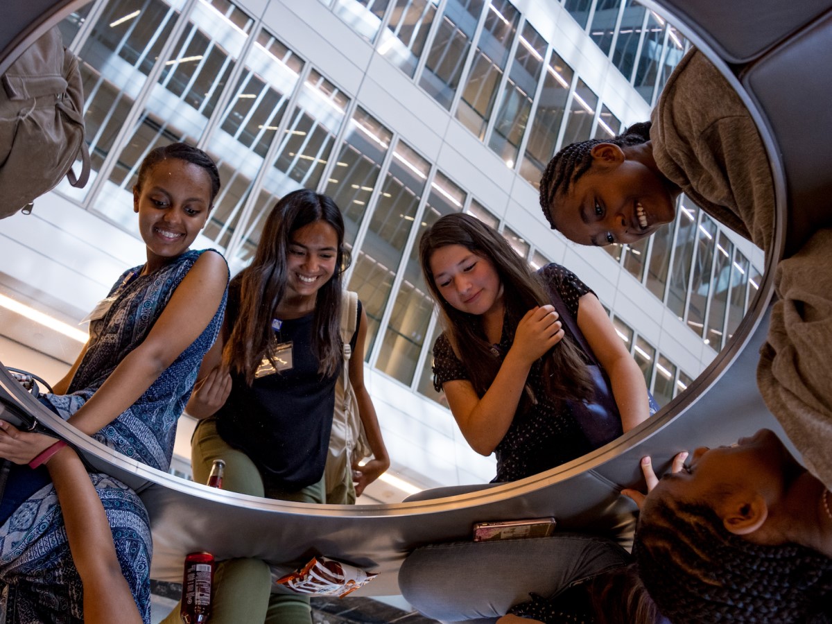four young people, gazing down into a reflective circle and seeing their images reflected back.