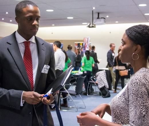 a young man with a tie and a nametag, talking to a woman about a job