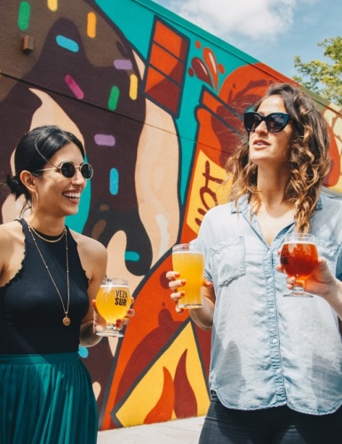 Young women toasting, standing in front of a mural