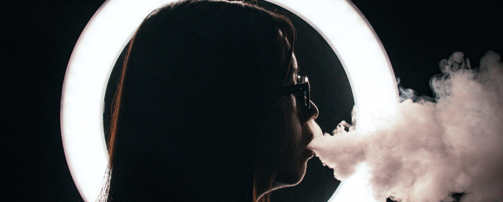 a woman in profile blowing smoke in front of a ring light
