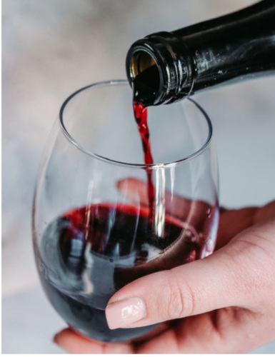 a hand holding a wine glass while a bottle pours red wine into it