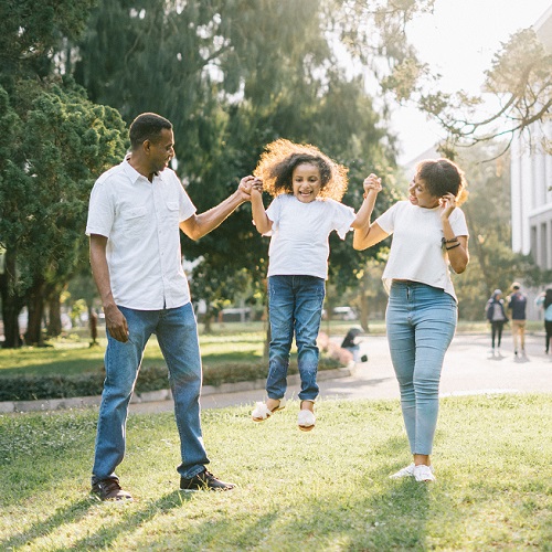 A man and a woman assisting a jumping girl, in a park