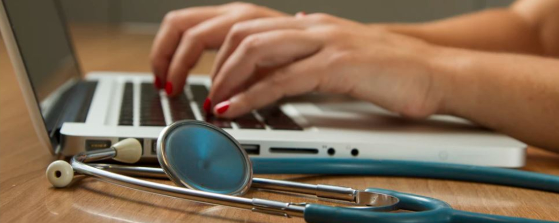 Hands typing on a laptop next to a stethoscope