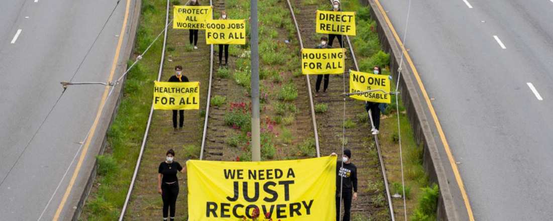 people in black on a grassy median in the middle of a holding bright yellow signs about economic rightsroad
