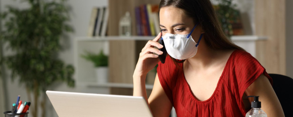 Woman on the phone in front of a computer, wearing a mask