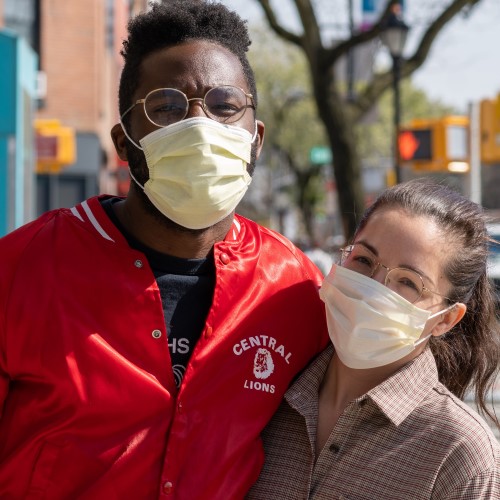 two people looking at camera, with arms around each other and masks. his jacket says lions