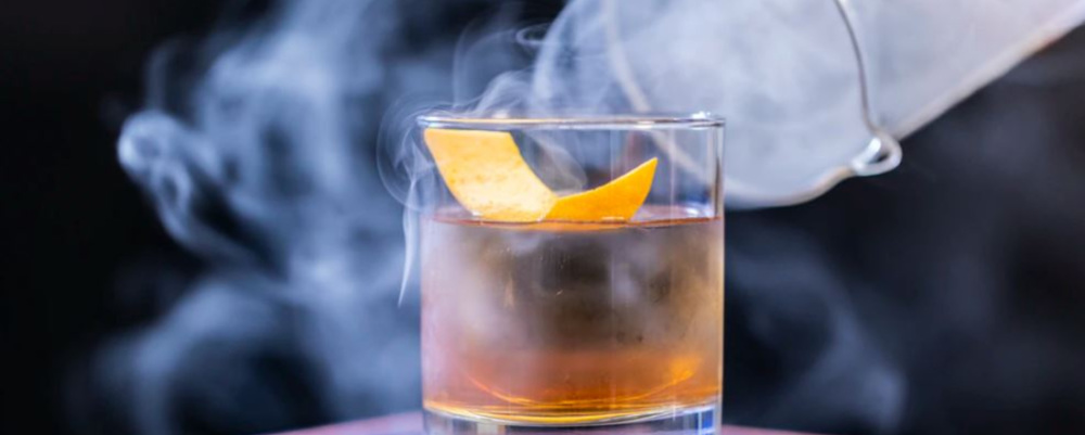 a drink glass filled with alcohol, surrounded by white smoke