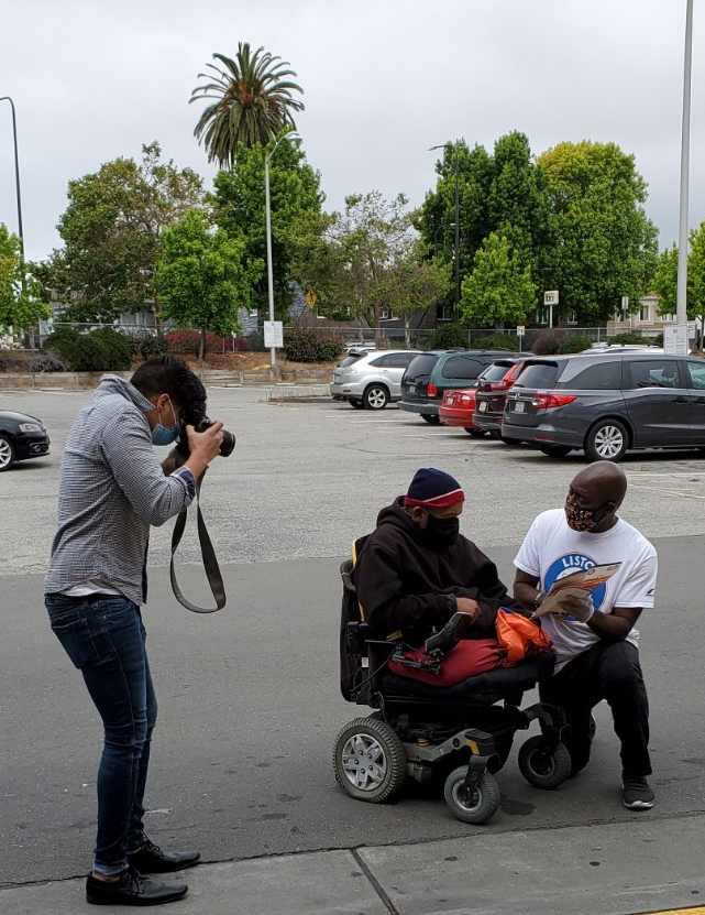 A photographer takes a photo of a Listos California worker showing resources to a person in a wheelchair
