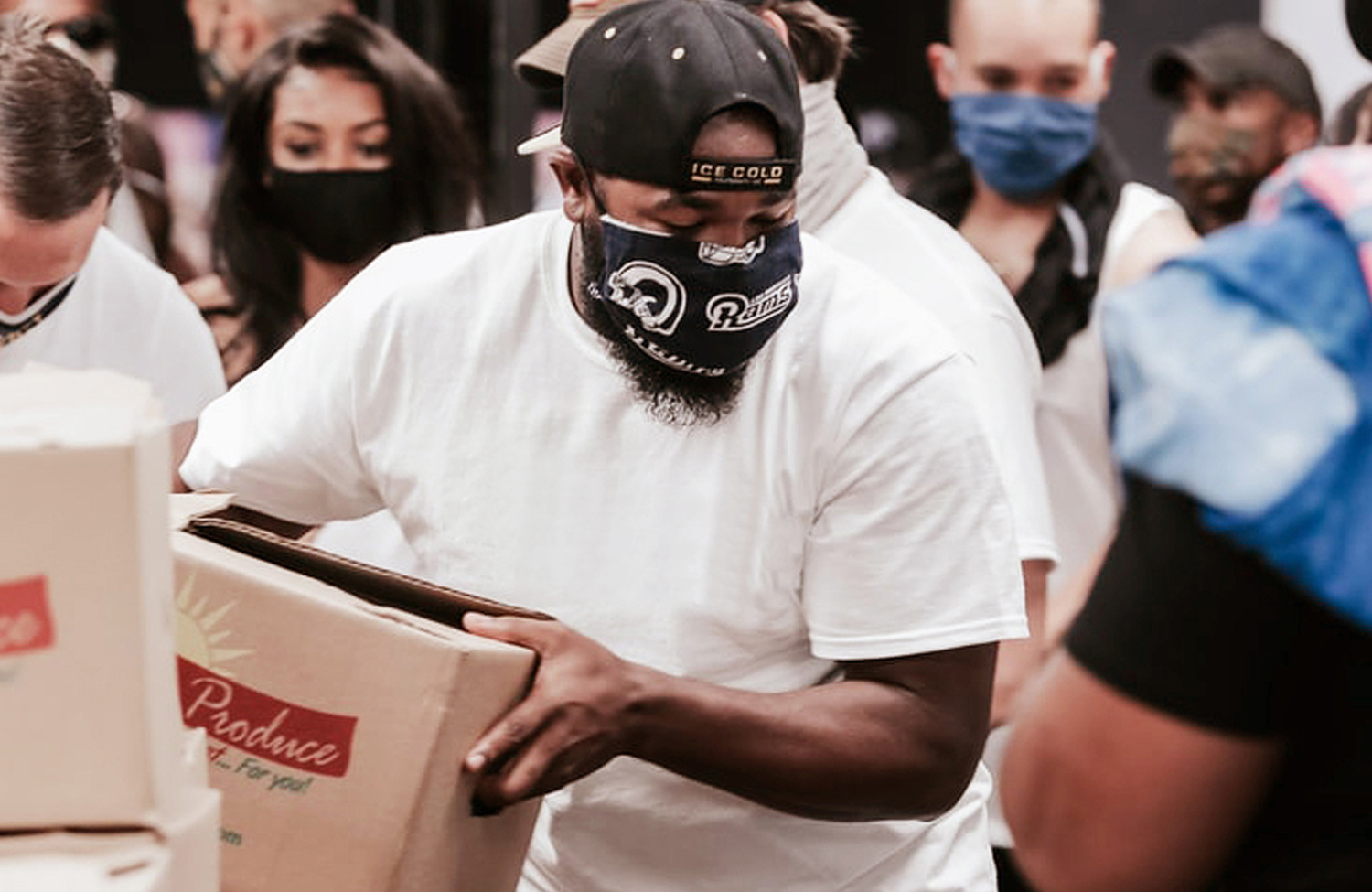 man wearing a face mask, holding box of produce