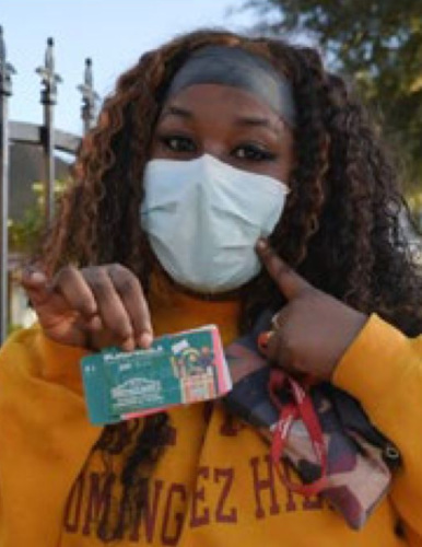 a young African American woman in a mask, holding up a food voucher card