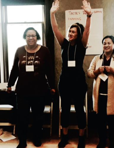 three women at a CACHI workshop, one with her hands up high