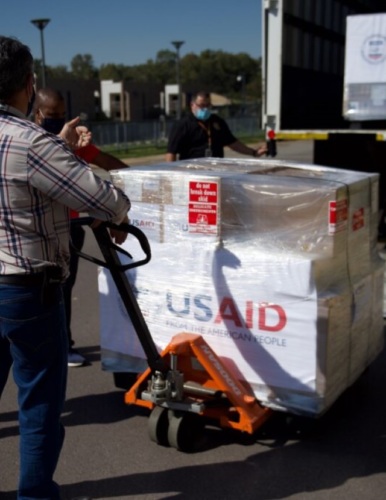 man pushing dolly load of ventilator boxes labeled USAID