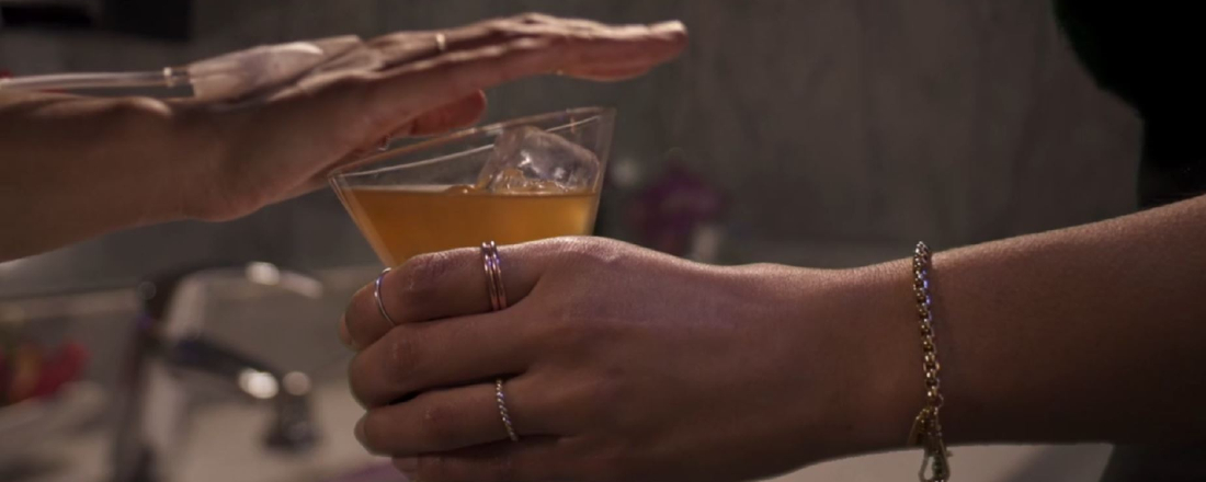 an extended hand holding an alcoholic drink while someone else hold's their hand over the top of it