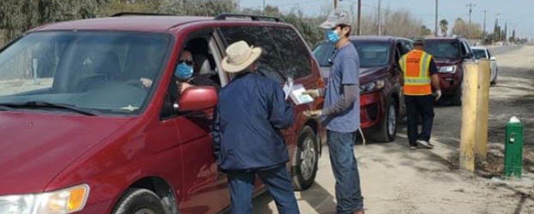 cars lined up for COVID testing while staff in masks hand out pamphlets