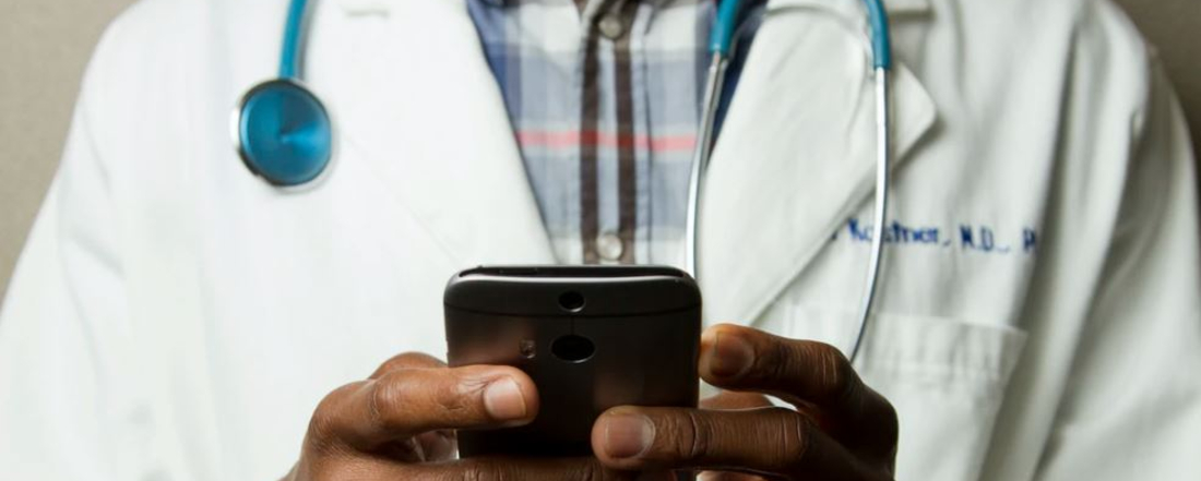 a doctor in a white lab coat looks at a smart phone