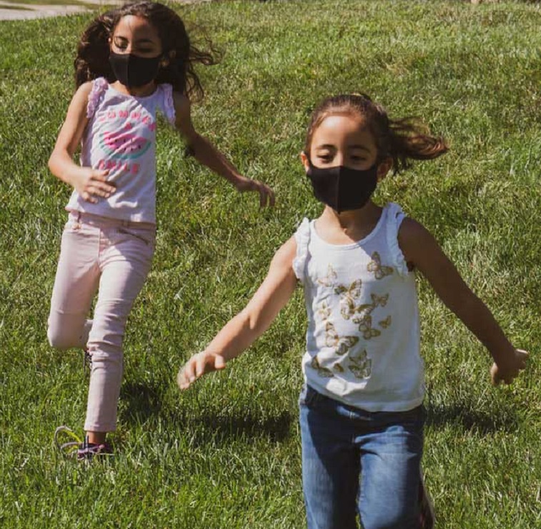 Two kids running and playing in a field, wearing masks