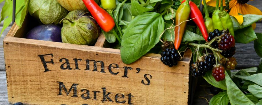 a wooden box of vegetables and black berries marked "Farmer's Market"