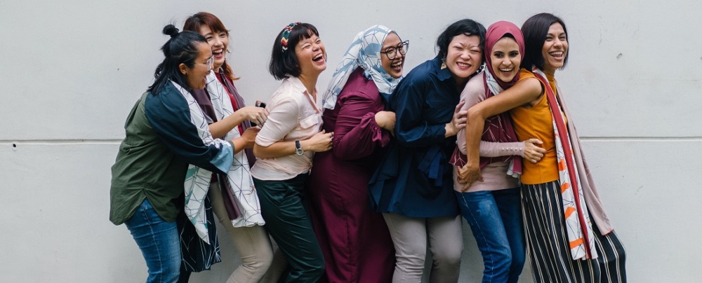 Women laughing in a row in front of a gray wall