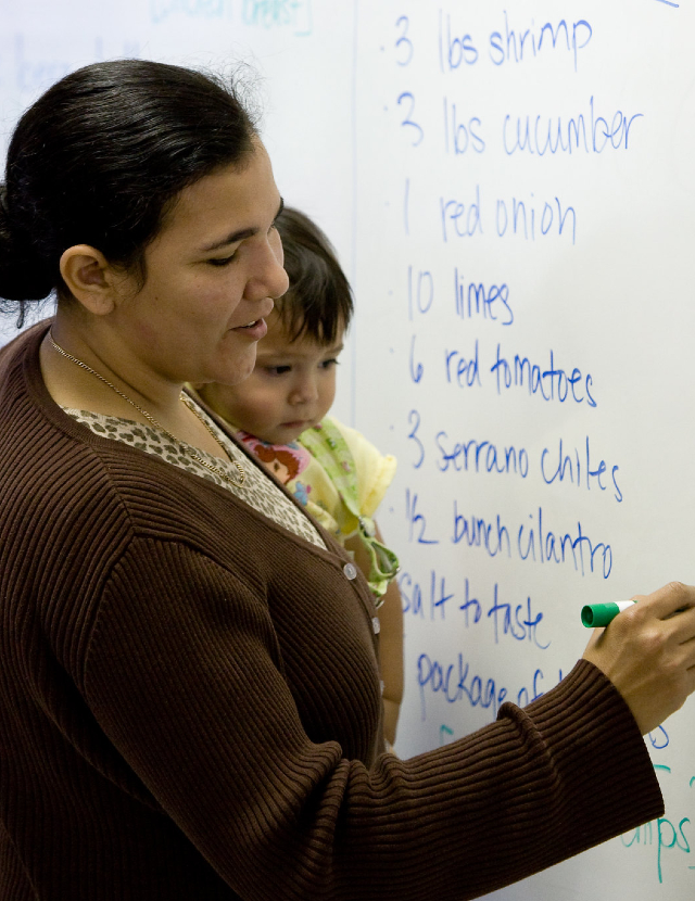 a woman holding a small child while writing on workshop paper on a wall