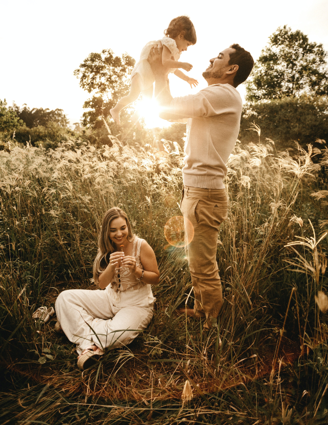 a family in tall grass, with the Dad holding up a small child