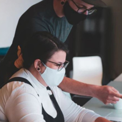 Man wearing face mask pointing at woman's computer