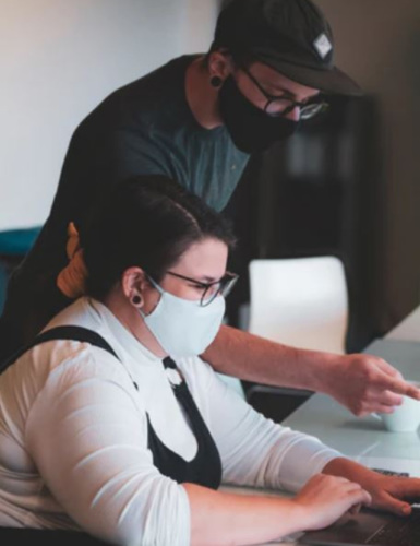 Man wearing face mask pointing at woman's computer