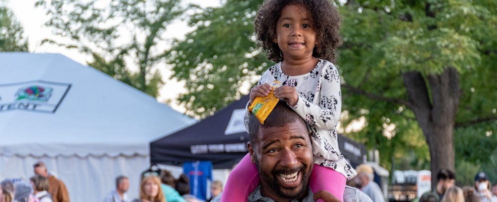 an African American dad at a festival with his child on his shoulders