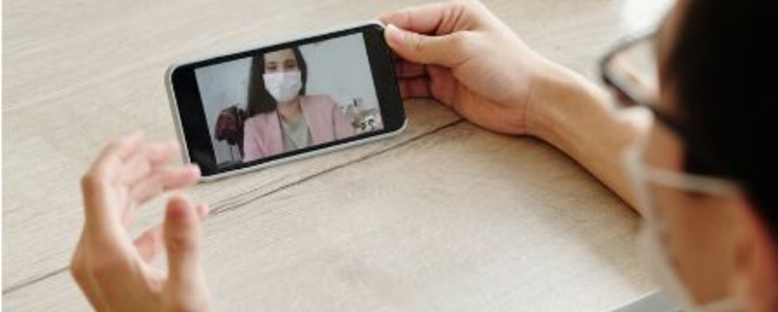 a patient in a mask looking at a doctor on cell phone