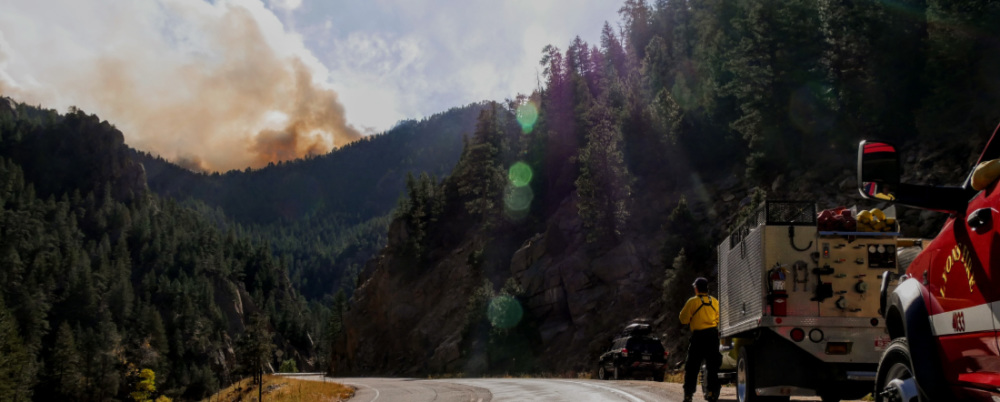 Firefighters by a roadside with wildfire smoke in the background