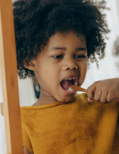a young African American child brushing their teeth in front of a mirror