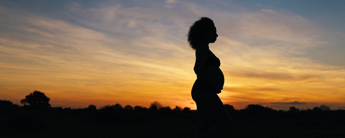 a silhouette of a pregnant woman with a sunset background