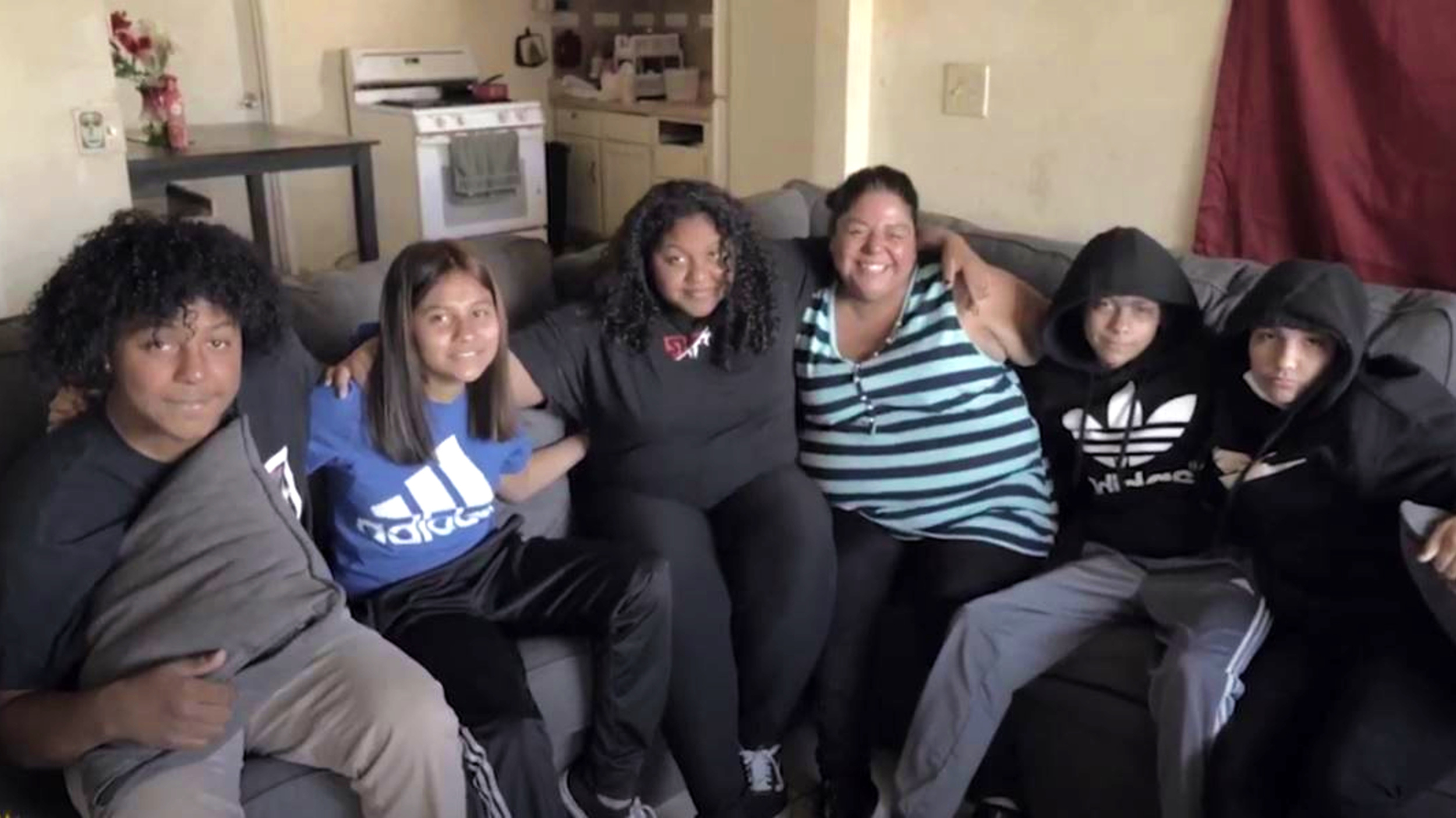 a woman and four teens on a couch with arms around each other