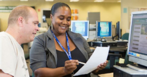 An African American woman showing notes to a colleague by a computer in a workplace