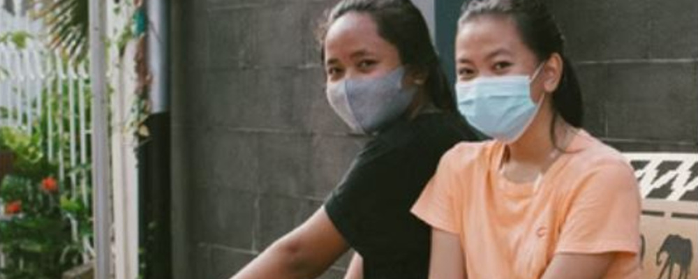 Two teens sitting together wearing medical masks