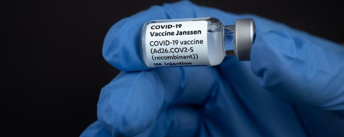 a blue-gloved hand holding a vial of Janssen COVID-19 vaccine